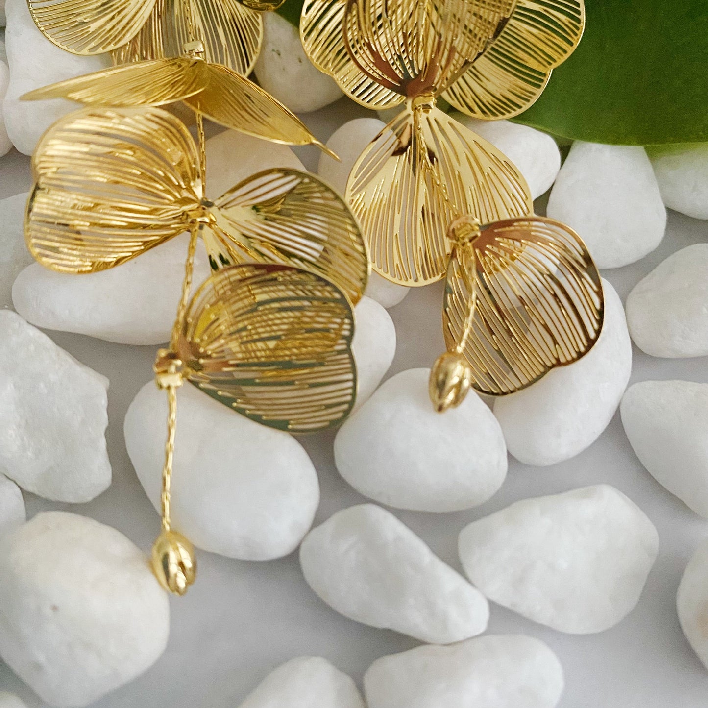 Gold leaf-shaped earrings on white pebbles