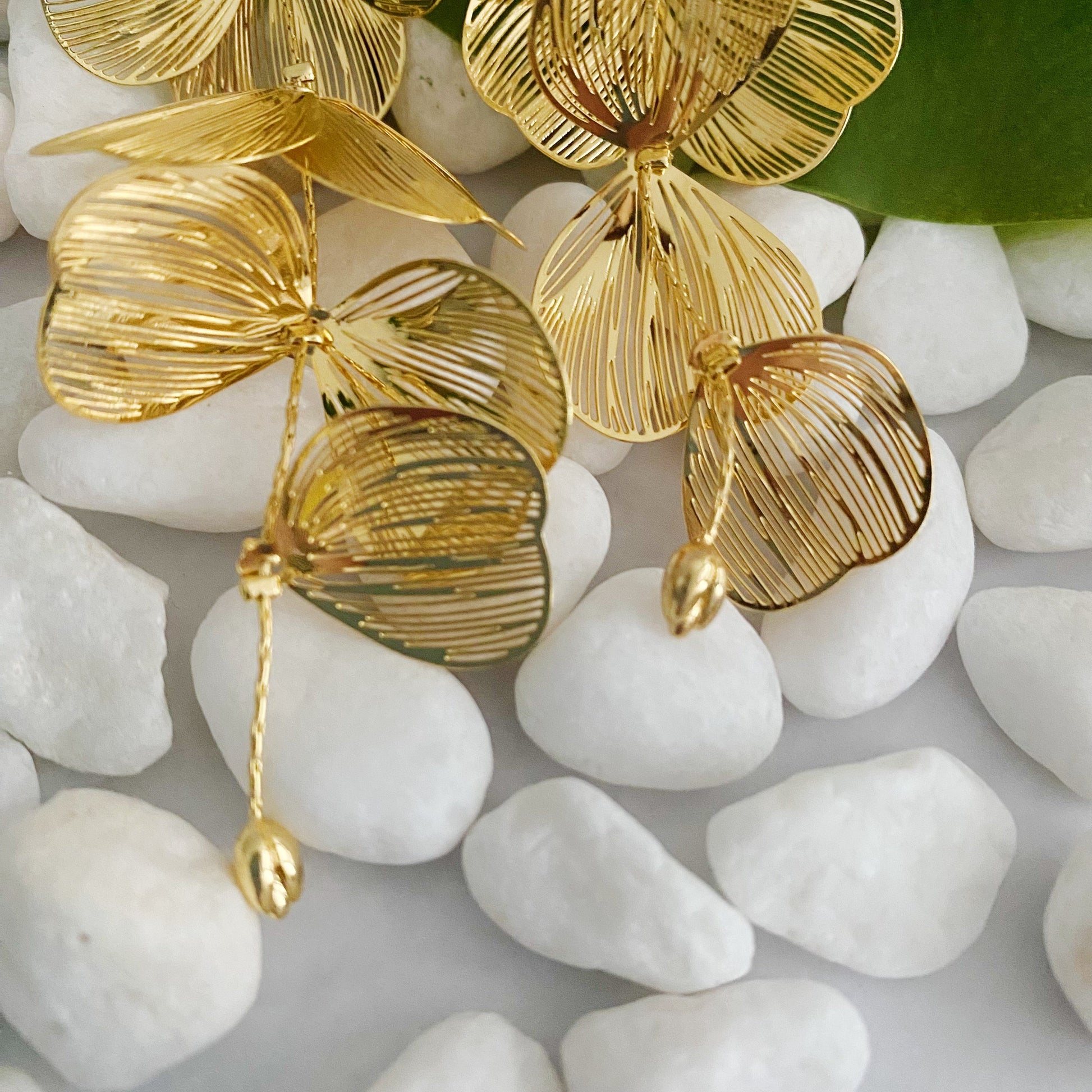 Gold leaf-shaped earrings on white pebbles