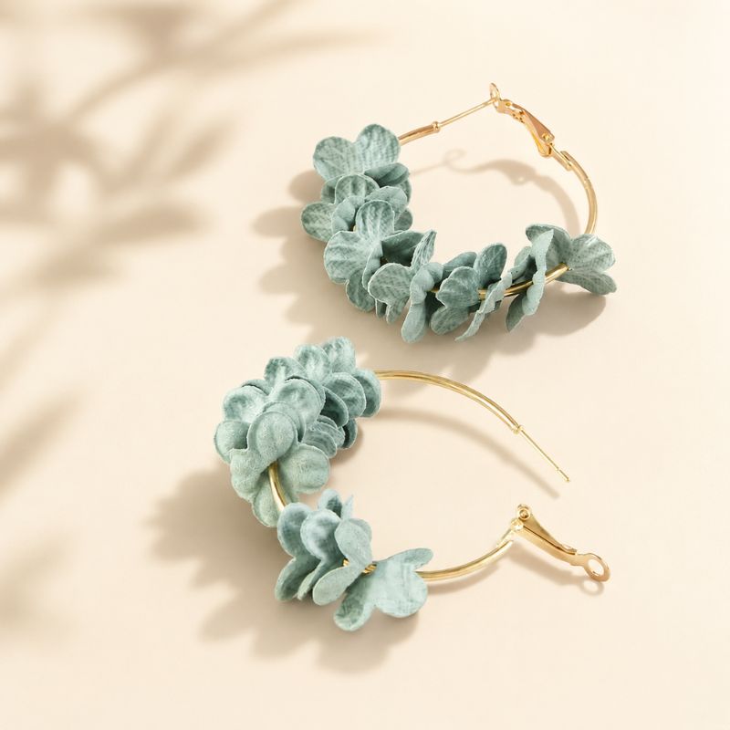 Pair of gold hoop earrings with green leaf-like decorations on a beige background