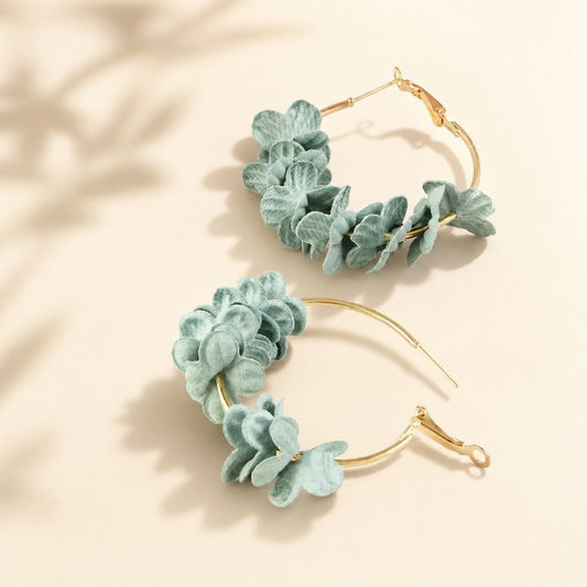 Pair of gold hoop earrings with green leaf-like decorations on a beige background