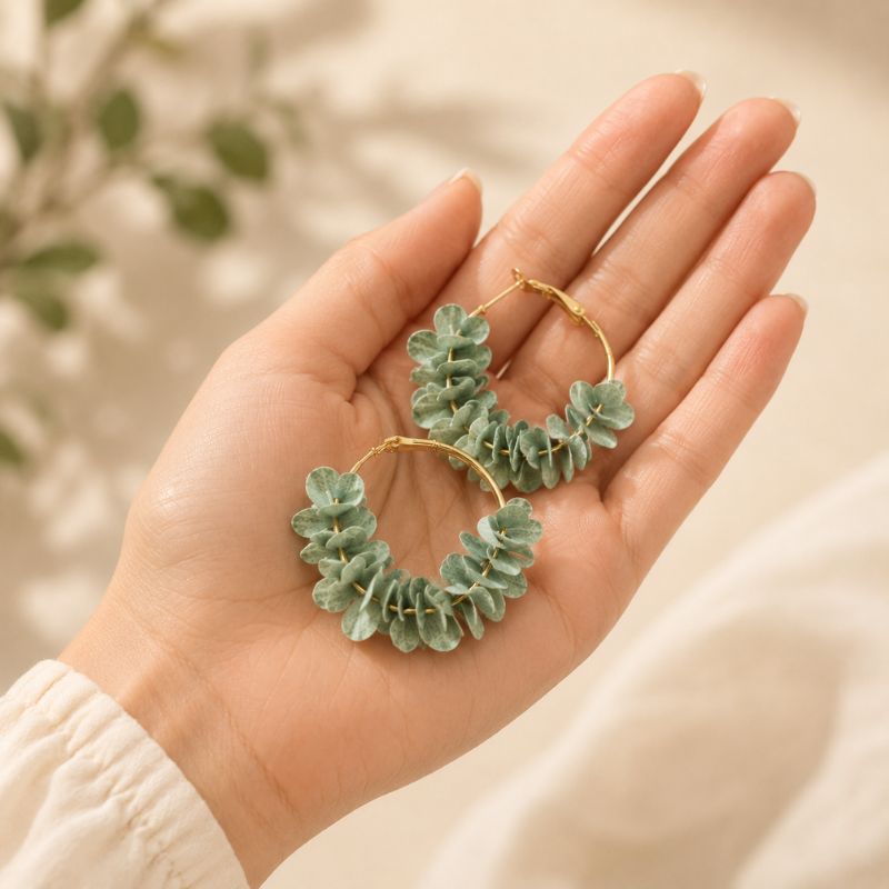 Hand holding a pair of light blue leaf-shaped earrings with a blurred natural background