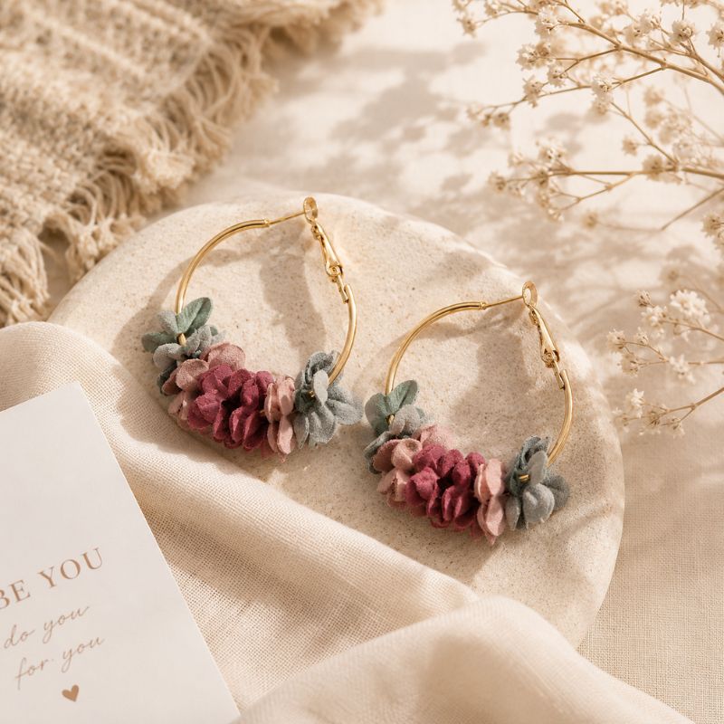 Gold hoop earrings with floral elements on a soft fabric background