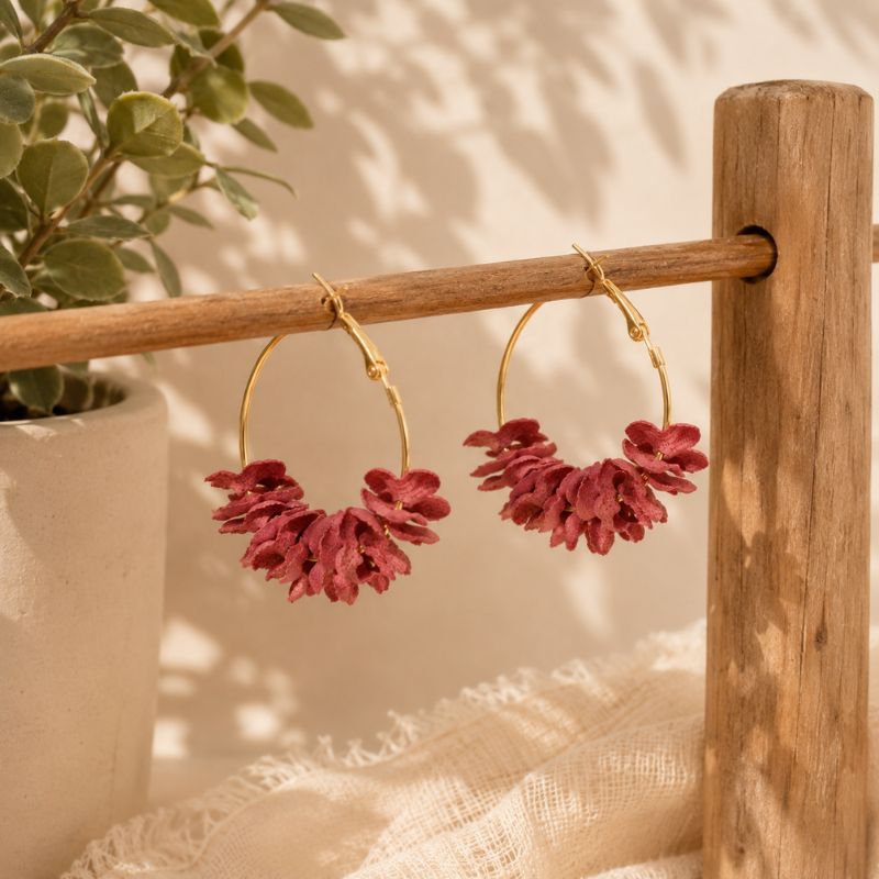 Gold hoop earrings with red floral attachments on a wooden stand with a plant in the background.