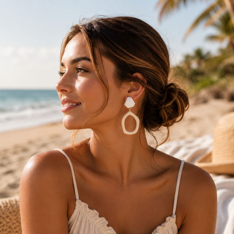 Woman on a beach wearing a white top and large earrings with a blurred background-Designs byBerniemae