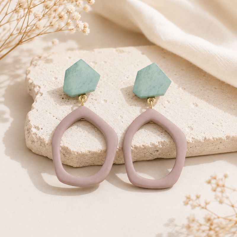 Pair of earrings with light blue gemstones and pinkish-purple loops on a textured surface.-Designs by Berniemae