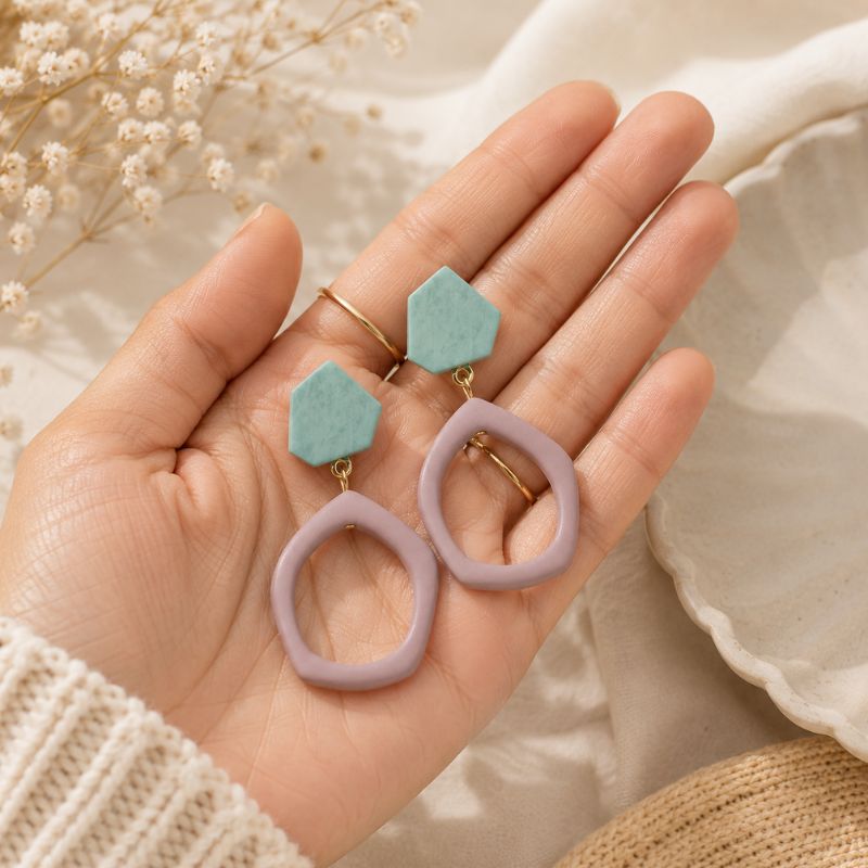 Hand holding two pairs of geometric earrings against a neutral background-Designs by Berniemae