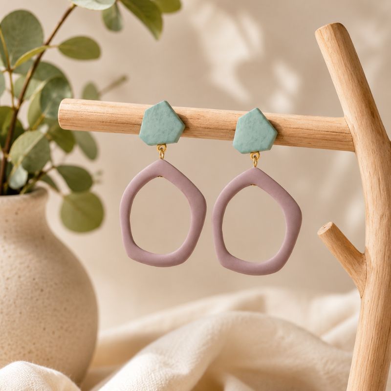 Pair of earrings with pink loops and green tops on a wooden stand with a natural background.-Designs by Berniemae