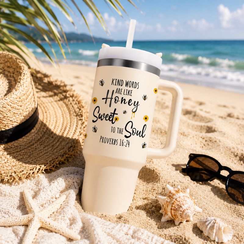 Beige tumbler with motivational quote on a sandy beach with a hat, sunglasses, and starfish.