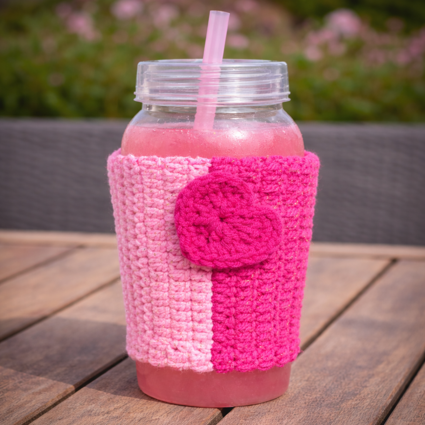 Pink crocheted drink sleeve on a glass jar with pink liquid and straw, outdoors.