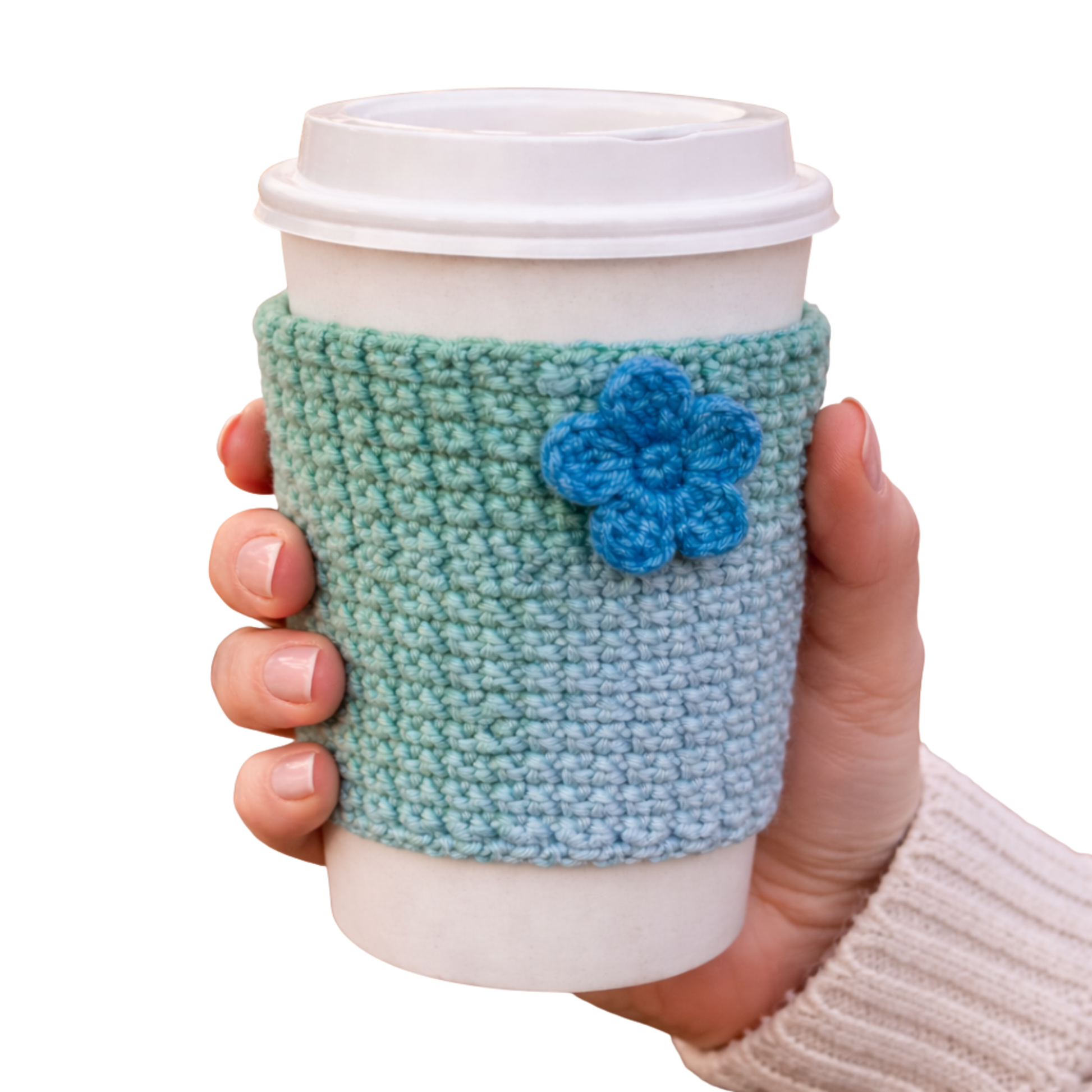 Hand holding a coffee cup with a green knitted sleeve and blue flower decoration on a white background