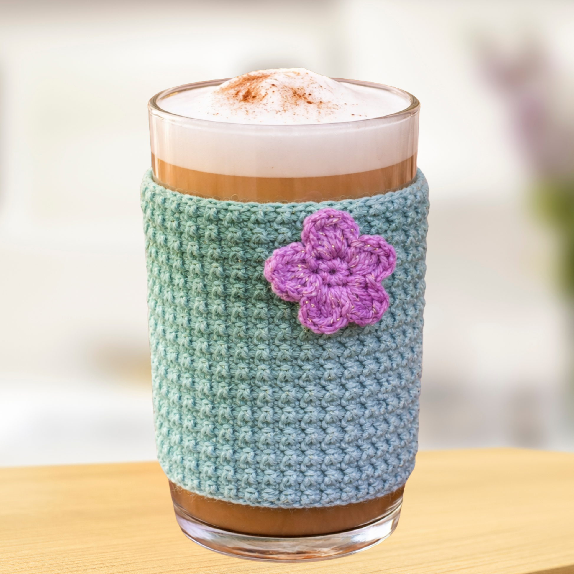 Peneli Luxe Glass of coffee with a teal sleeve and purple flower on a wooden surface