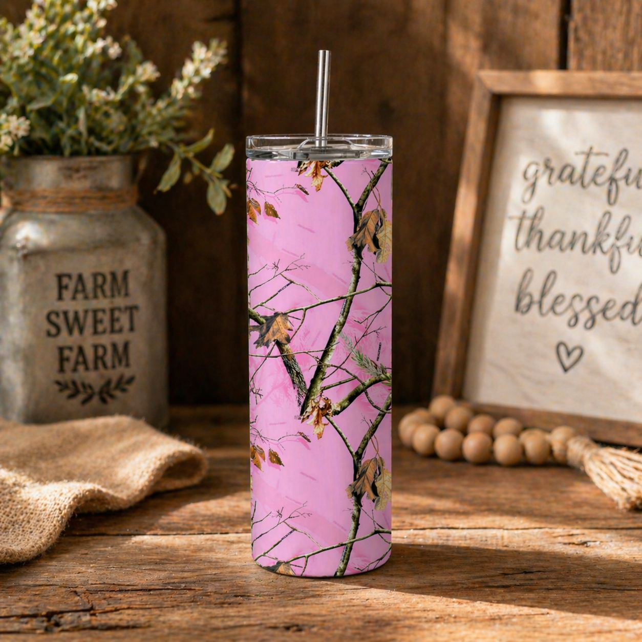 Pink camo-patterned tumbler with a straw on a wooden surface, with 'Farm Sweet Farm' sign and rustic decor in the background.