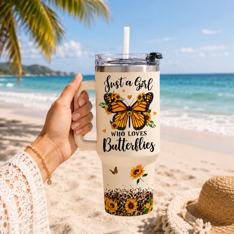 Person holding a tumbler with butterfly design on a beach