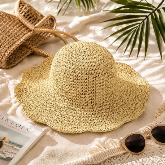 Beige straw hat on a white surface with sunglasses and a magazine underneath, surrounded by green leaves.-Designs by Berniemae