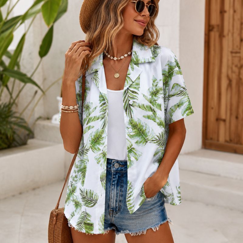 Woman wearing a tropical print shirt over a white top and denim shorts, standing outdoors.-Designs by Berniemae